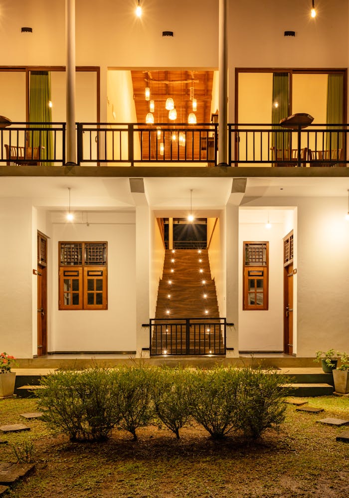Charming two-story outdoor view with warm, inviting lighting and lush greenery.