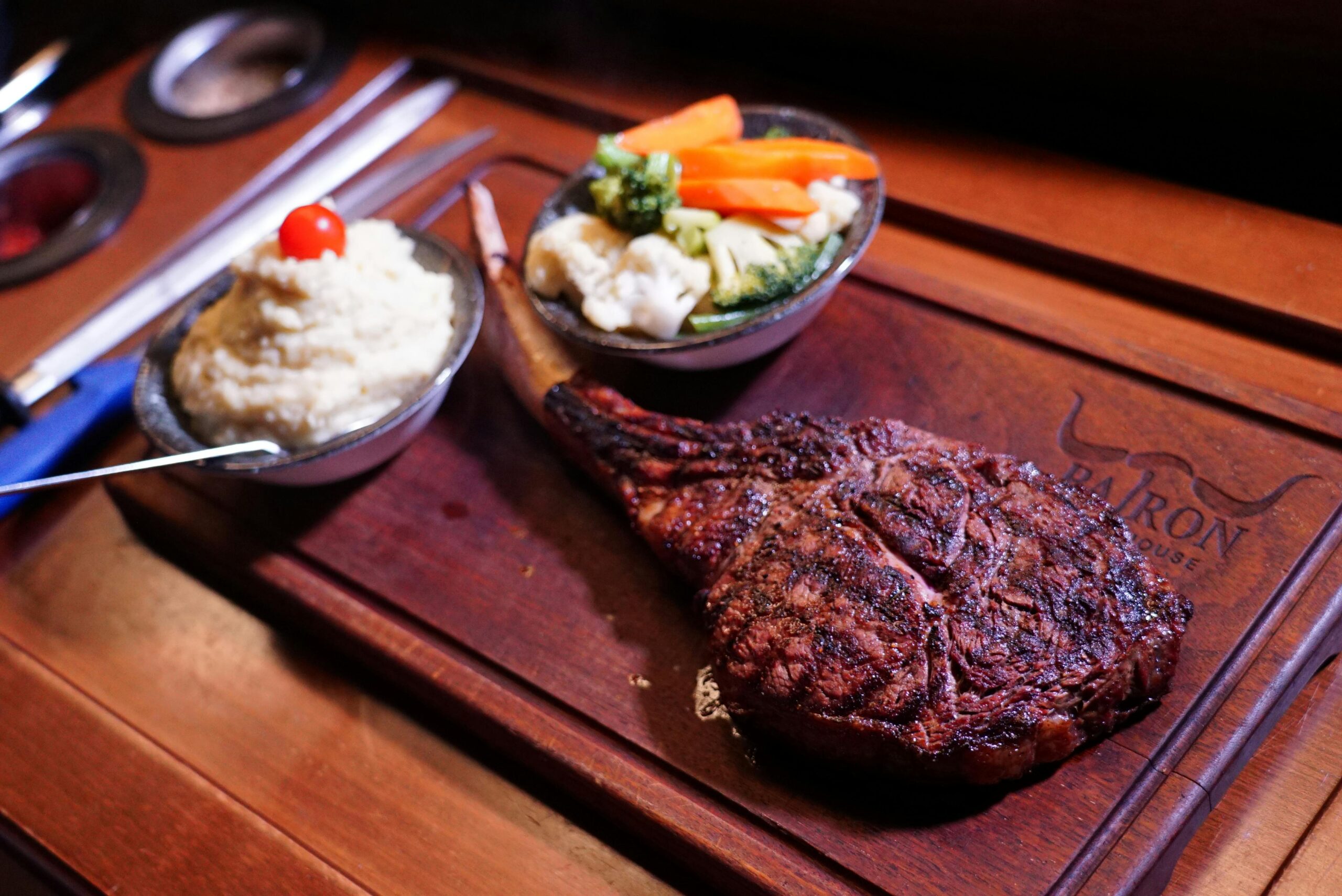 A delicious tomahawk steak served with mashed potatoes and mixed vegetables on a wooden platter.